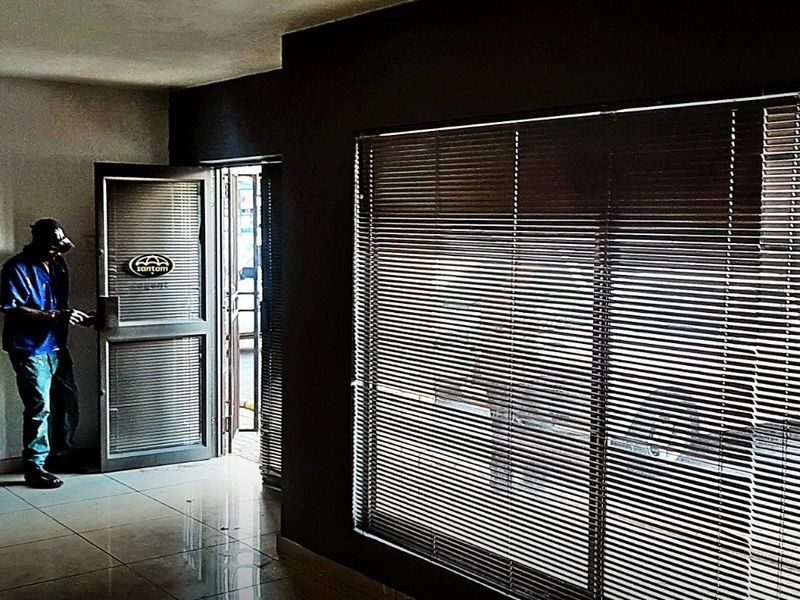 An empty retail entrance area featuring tiled flooring, large windows with venetian blinds, and an aluminium framed glass door.