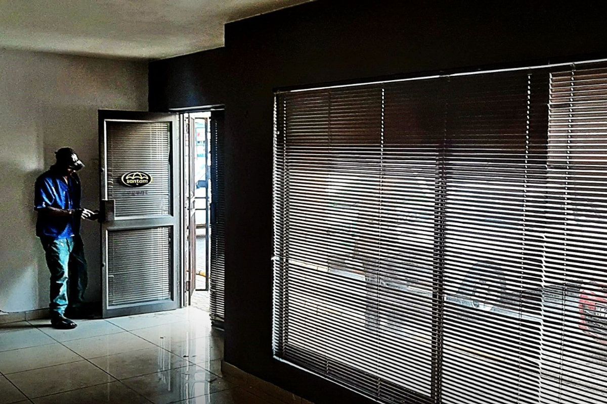 An empty retail entrance area featuring tiled flooring, large windows with venetian blinds, and an aluminium framed glass door.