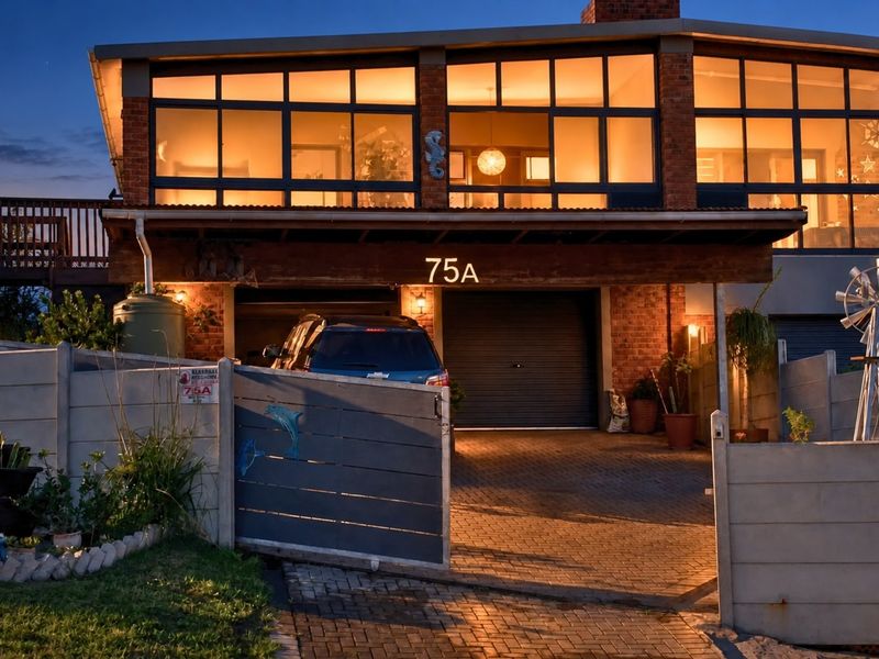 Front elevation of a duet property featuring a brick facade, large windows, double garage, and a paved driveway with secure gated access.