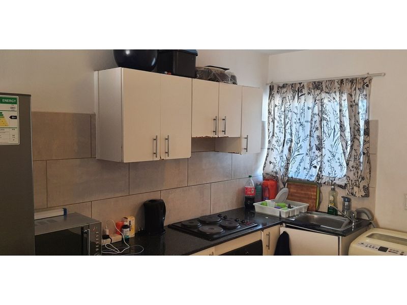 Compact kitchen featuring built-in cabinetry, granite countertops, an electric hob, and a stainless steel sink with tiled backsplash.