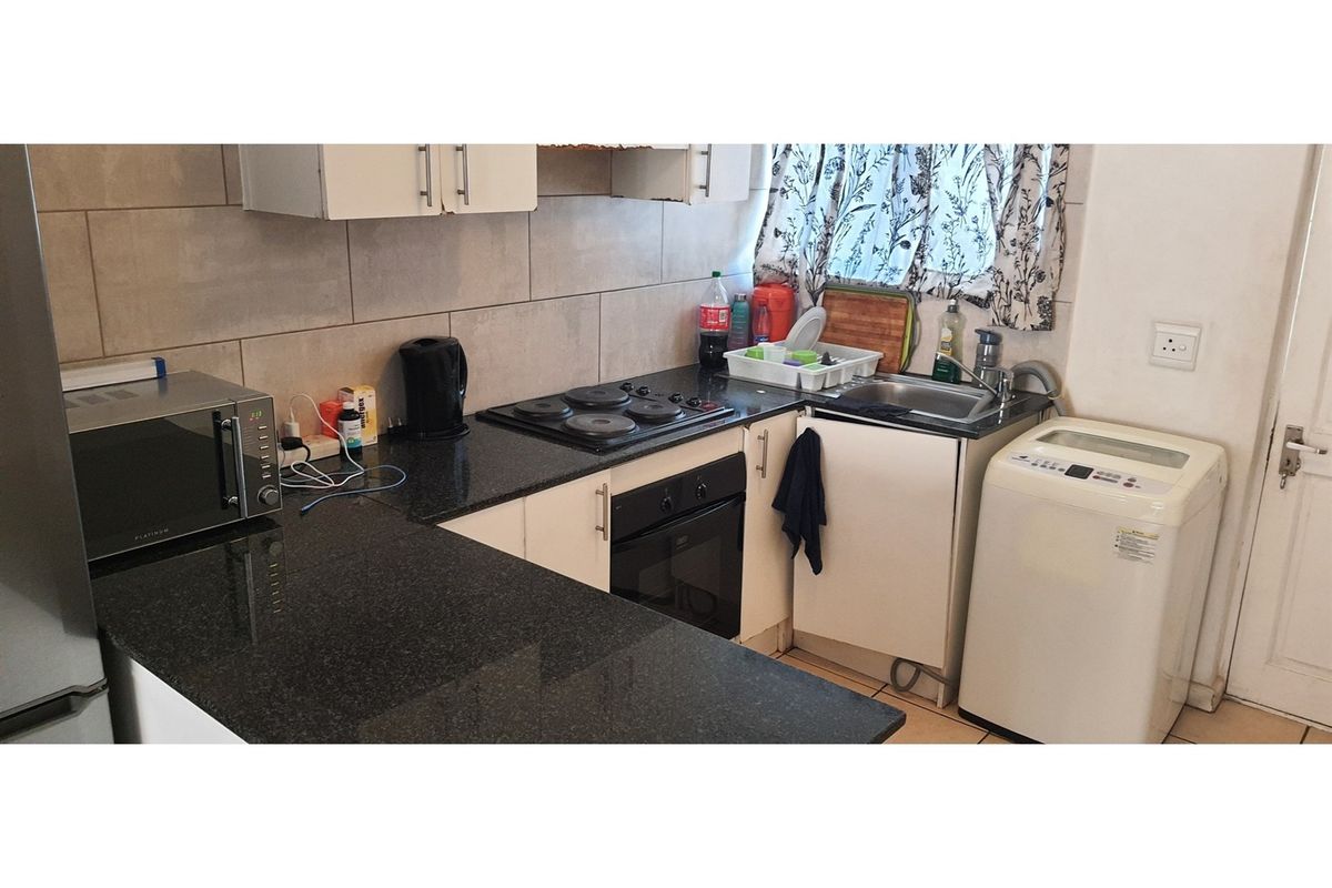 Compact kitchen featuring granite countertops, built-in cabinetry, an electric hob, oven, and a stainless steel sink with tiled backsplash.