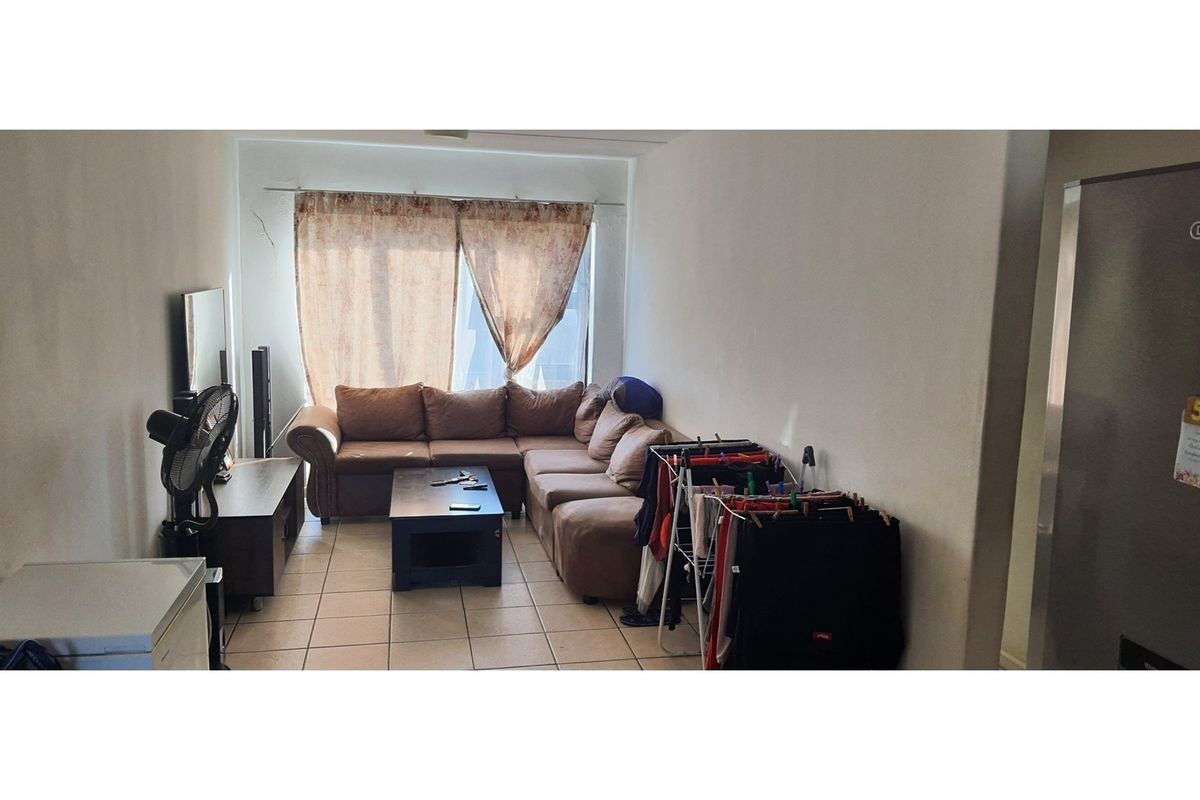 A living room area featuring tiled flooring and a large window with curtain fittings, showing signs of wear including a visible wall crack.