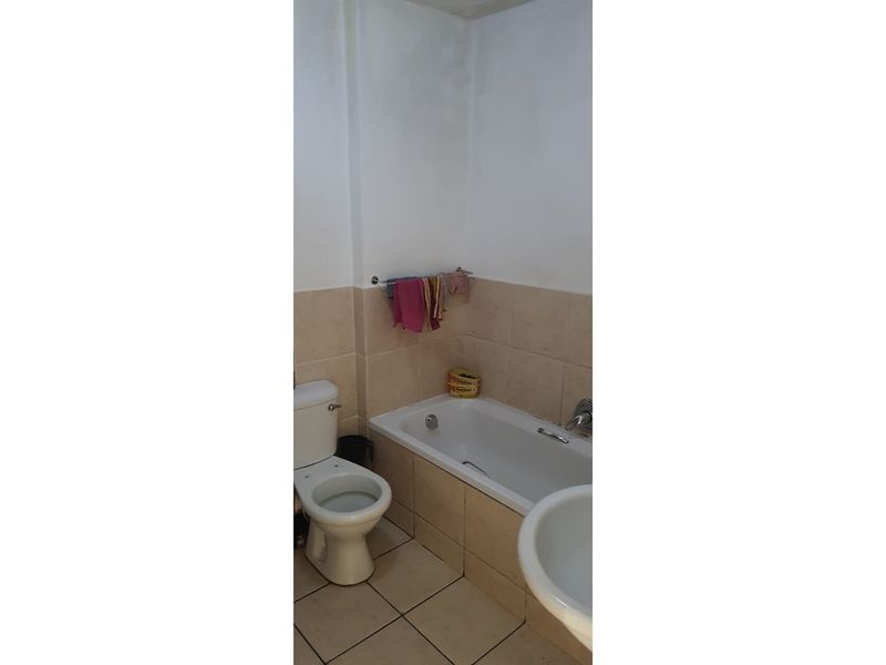 A functional bathroom featuring a standard bathtub, toilet, and pedestal basin with neutral wall and floor tiling.