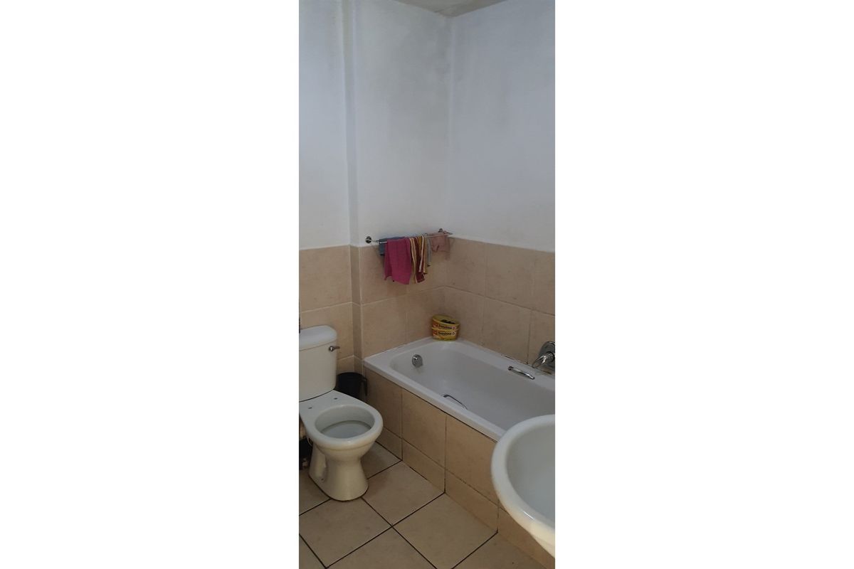 A functional bathroom featuring a standard bathtub, toilet, and pedestal basin with neutral wall and floor tiling.