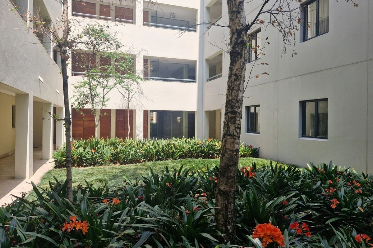 A well-maintained central courtyard garden featuring lush landscaping and mature trees, surrounded by the apartment building's facade with private balconies.
