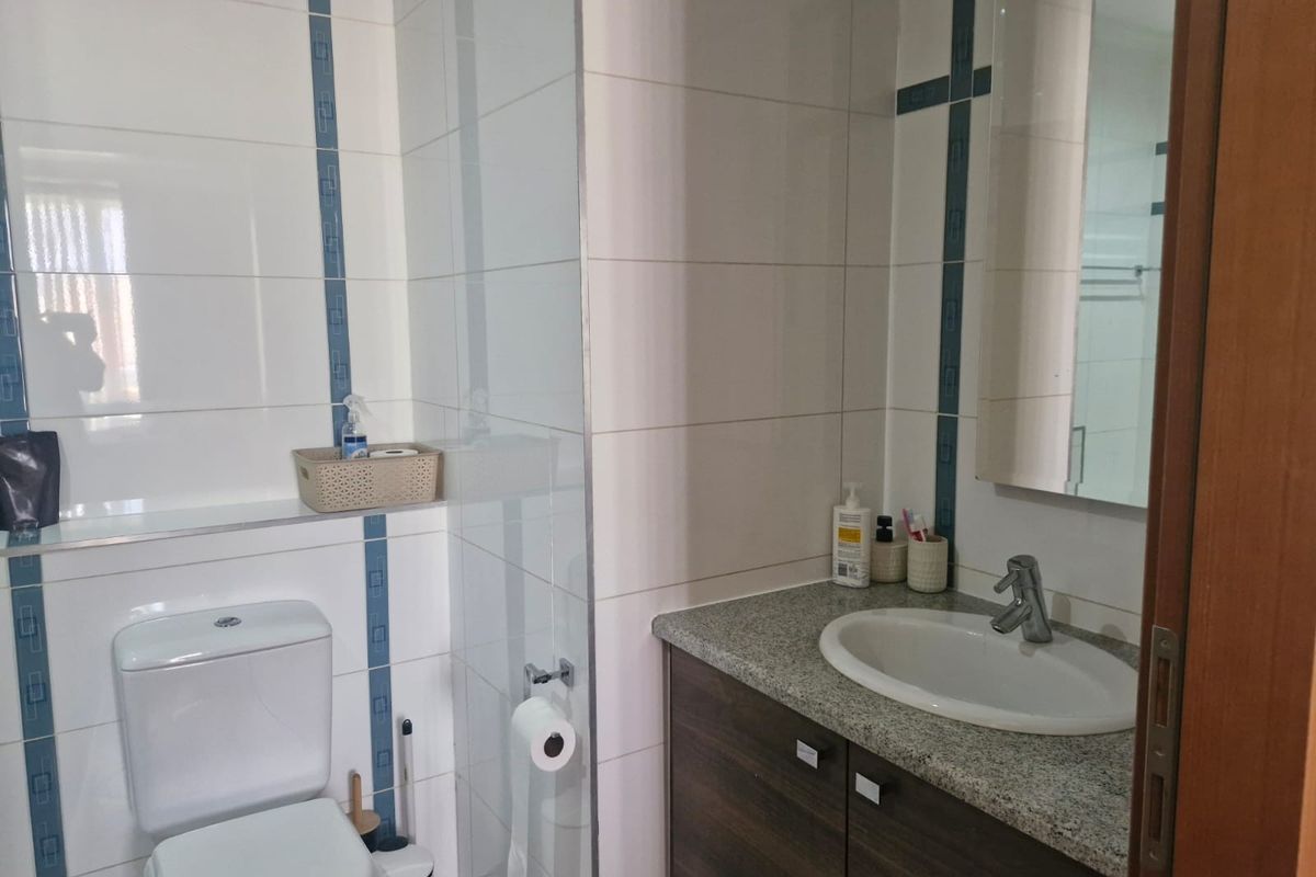 A functional bathroom featuring a vanity with granite countertop, inset sink, toilet, and a glass shower screen with tiled wall finishes.