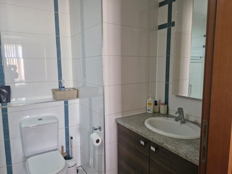 A functional bathroom featuring a vanity with granite countertop, inset sink, toilet, and a glass shower screen with tiled wall finishes.