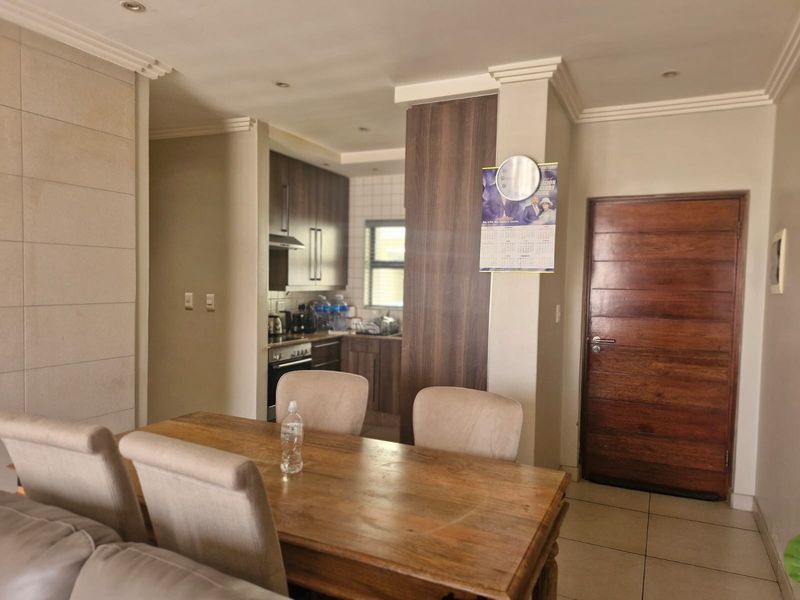 Open-plan living and dining area featuring tiled floors, a stone feature wall, and a functional kitchen with built-in cabinetry and integrated appliances.