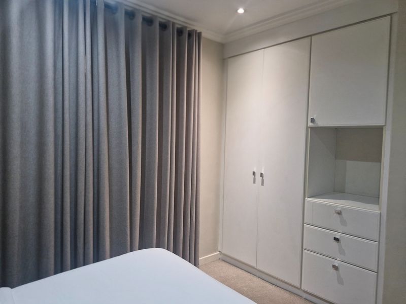 A well-maintained bedroom featuring neutral carpeted flooring, recessed ceiling lighting, and ample built-in cupboard storage with integrated drawers.