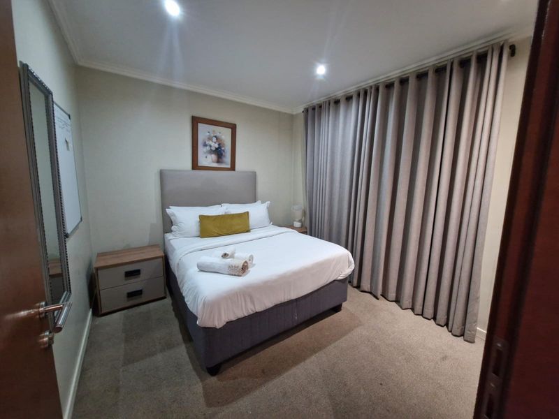 A well-maintained bedroom featuring neutral wall tones, recessed ceiling lighting, and full-length curtains providing privacy and a soft aesthetic.