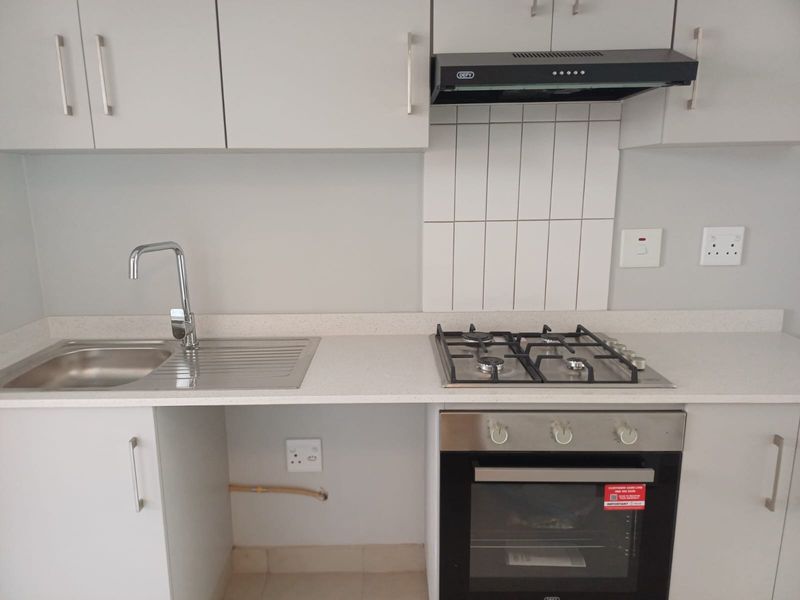 Modern kitchen featuring light grey cabinetry, stone countertops, a stainless steel sink, gas hob, built-in oven, and a sleek tiled splashback.