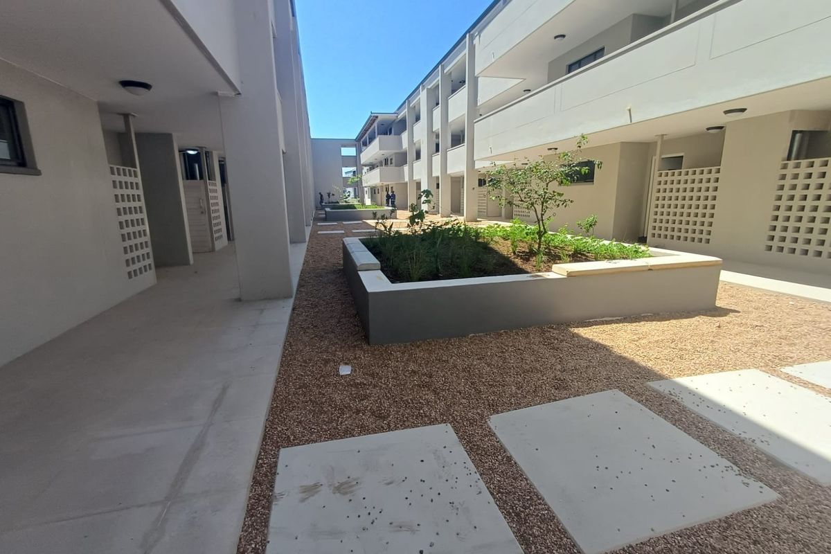 A well-maintained apartment complex courtyard featuring gravel landscaping, raised garden beds, concrete pavers, and covered walkways with breeze block architectural details.