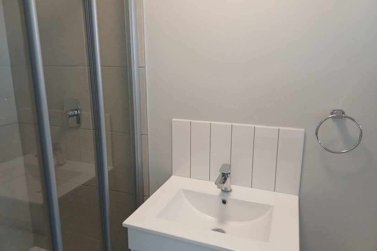 A clean, modern bathroom featuring a vanity basin with a mixer tap, tiled splashback, and a glass-enclosed shower.