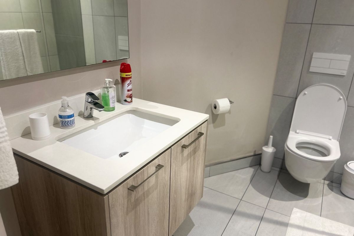 Modern bathroom featuring a wood-finish vanity with integrated basin, wall-mounted mirror, and a wall-hung toilet with concealed cistern, finished with neutral floor tiles.