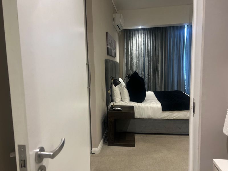 A well-maintained bedroom featuring carpeted flooring, a built-in cupboard, and an integrated air conditioning unit, viewed from the doorway.