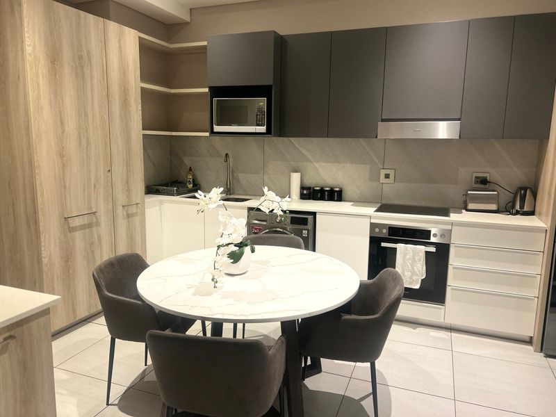 Modern open-plan kitchen featuring sleek two-tone cabinetry, integrated appliances, stone splashback, and high-quality tiled flooring, seamlessly flowing into the dining area.