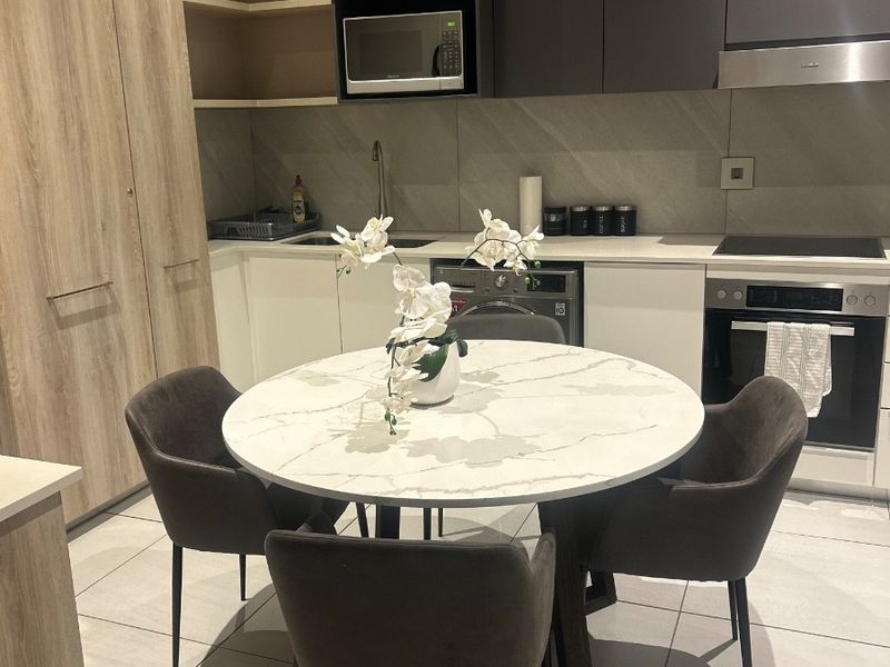Modern open-plan kitchen featuring sleek two-tone cabinetry, integrated appliances, stone countertops, and large format floor tiles in a contemporary apartment setting.