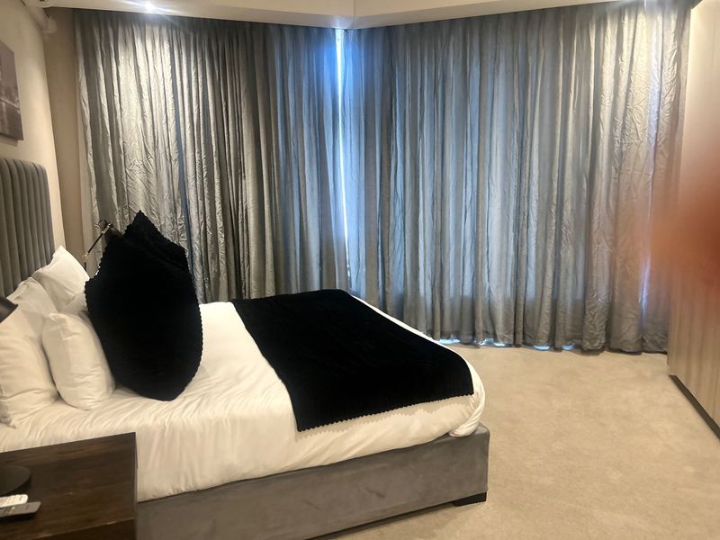 A well-maintained bedroom featuring floor-to-ceiling curtains, neutral carpeting, and built-in wardrobe storage.