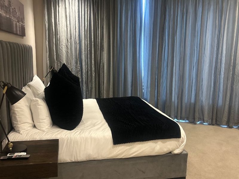 A well-maintained bedroom featuring neutral carpeting, wall-mounted air conditioning, and floor-to-ceiling curtains providing a soft, finished aesthetic.