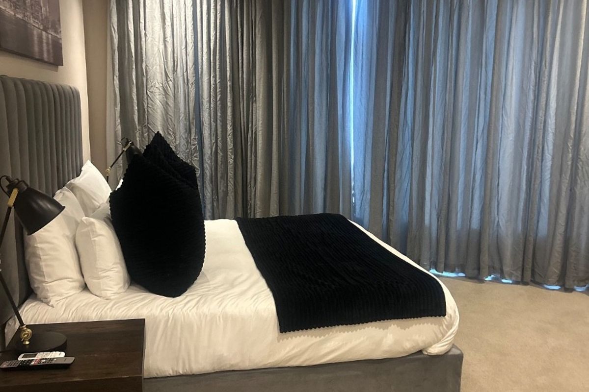 A well-maintained bedroom featuring neutral carpeting, wall-mounted air conditioning, and floor-to-ceiling curtains providing a soft, finished aesthetic.