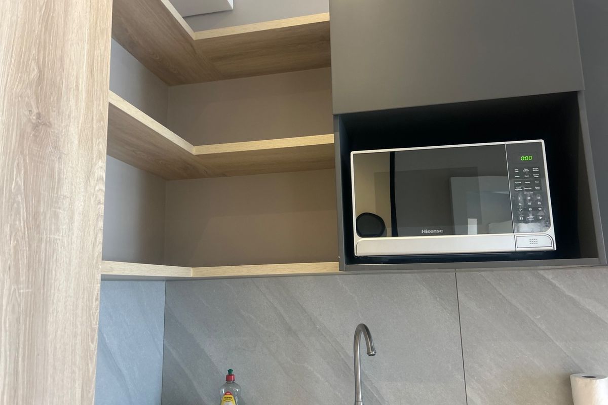 Modern kitchen area featuring sleek grey cabinetry, open wood-tone shelving, a built-in microwave, and a contemporary stone tile backsplash with a stainless steel sink.