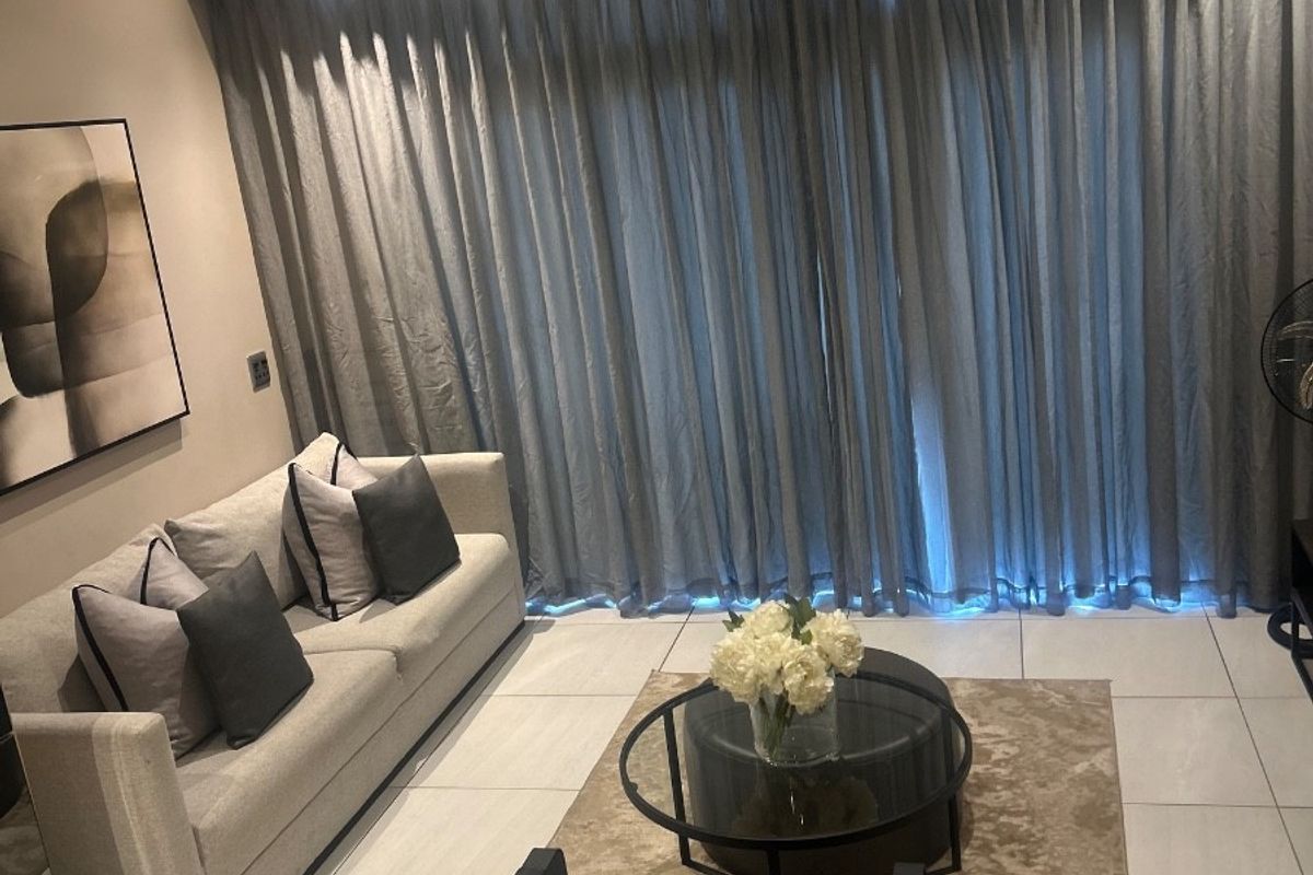 A modern living room featuring neutral tiled flooring, recessed ceiling lighting, and full-length curtain tracks, creating a clean and contemporary atmosphere.