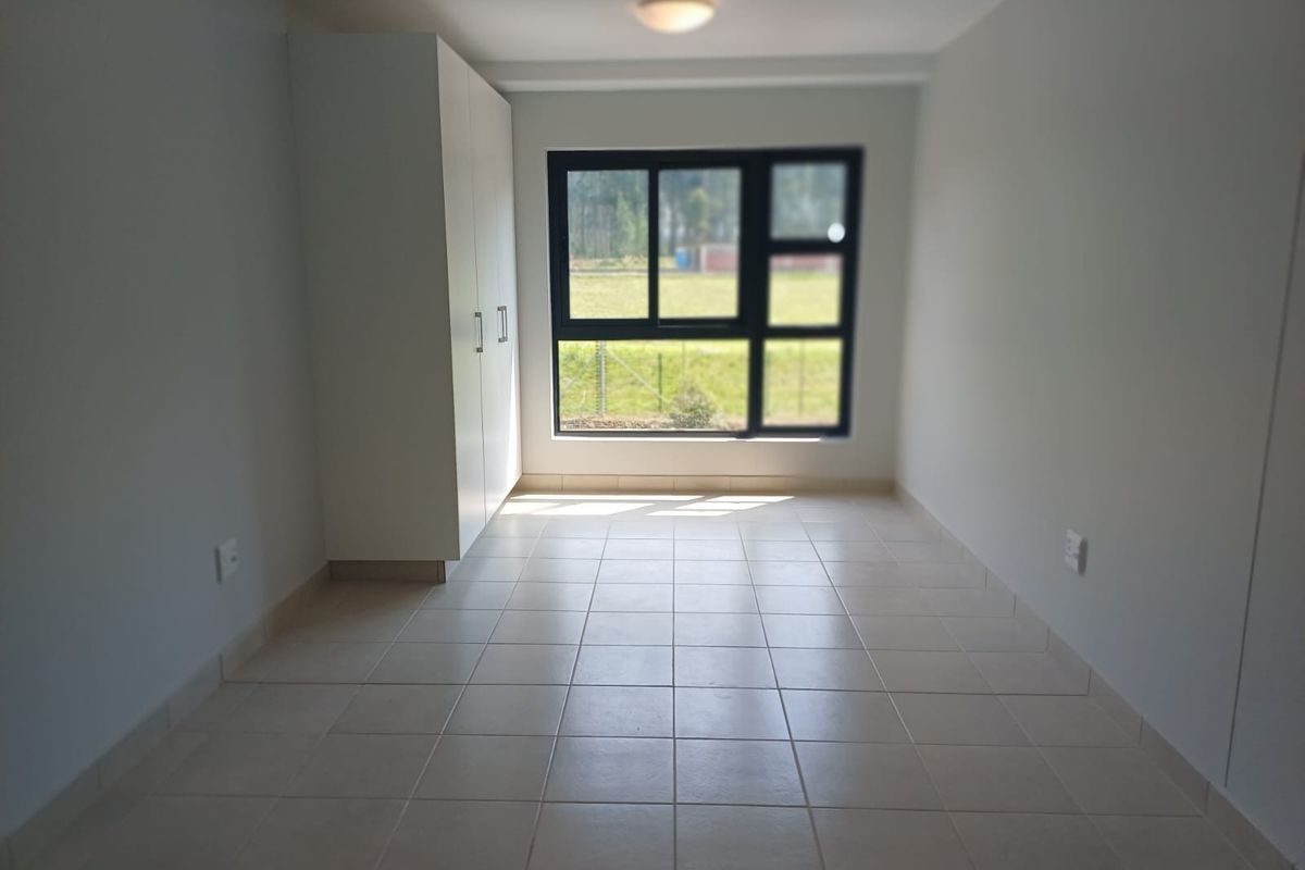 A clean, empty bedroom featuring neutral tiled flooring, a built-in wardrobe, and a large window providing natural light.