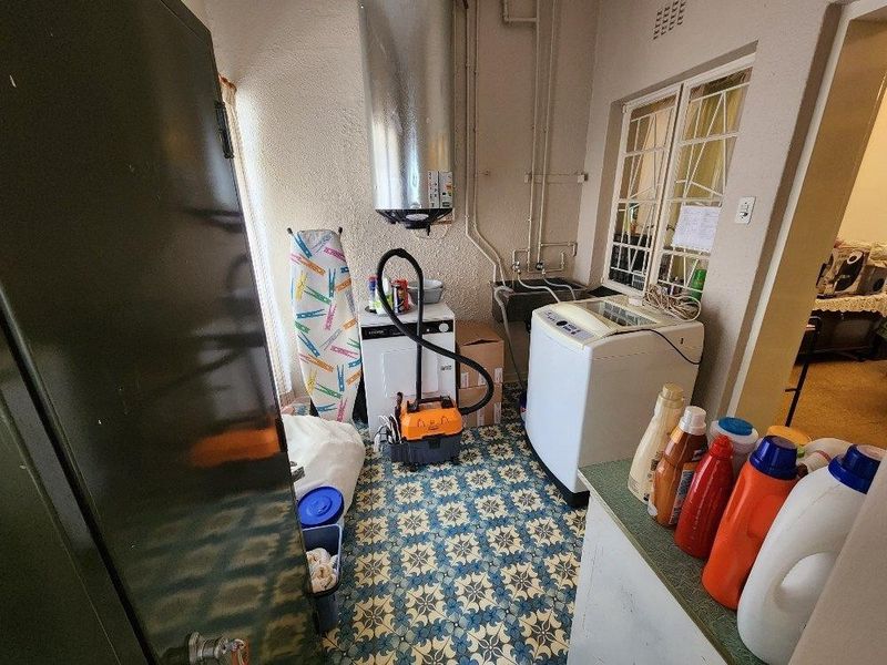 Functional laundry room featuring a utility sink, wall-mounted electric water heater, and patterned floor tiles.