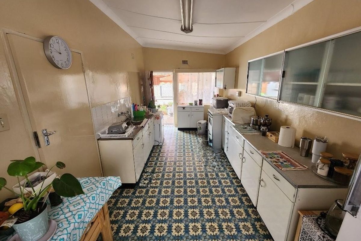 A functional, dated kitchen featuring original cabinetry, patterned tile flooring, and direct access to the rear exterior area.