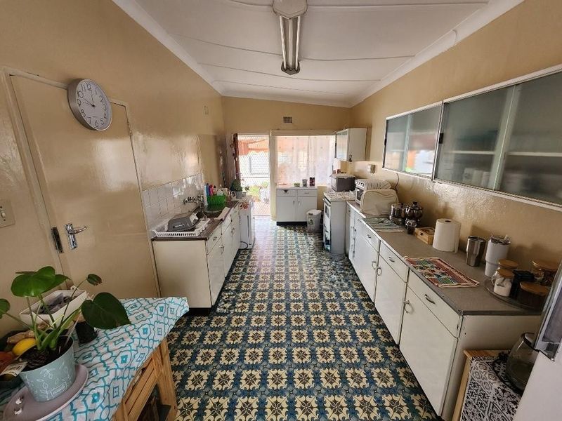 A functional, dated kitchen featuring original cabinetry, patterned tile flooring, and direct access to the rear exterior area.