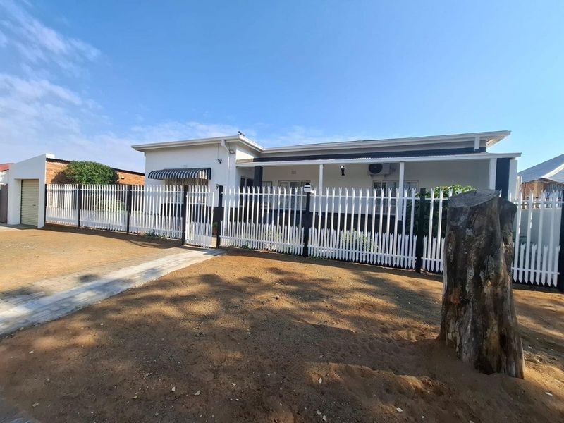 Front view of a single-story house featuring a white metal picket fence, a paved driveway, a single garage, and a covered front porch.