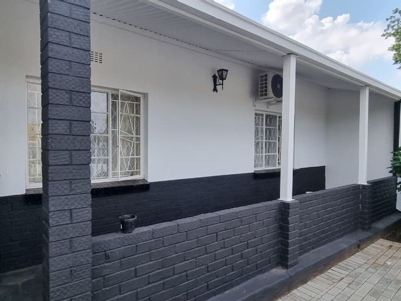 A covered patio area featuring paved flooring, a security gate, and an installed air conditioning unit against a freshly painted exterior wall.