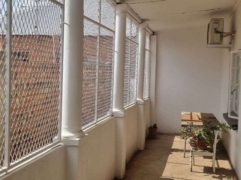A covered patio area featuring security mesh enclosures, structural columns, and an installed air conditioning unit, offering a functional outdoor space.