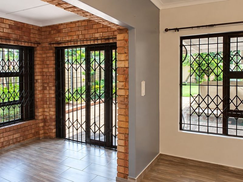 Bright living area featuring exposed brick walls, tiled flooring, and secure metal gates on windows and sliding doors leading to the garden.