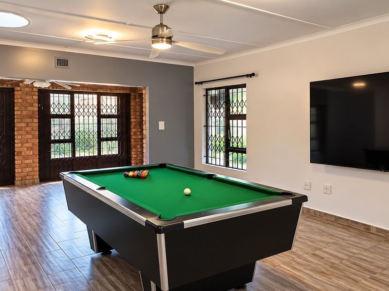 Spacious living area featuring tiled flooring, exposed brick accents, a ceiling fan, and secure access points, currently utilized as a recreational space.