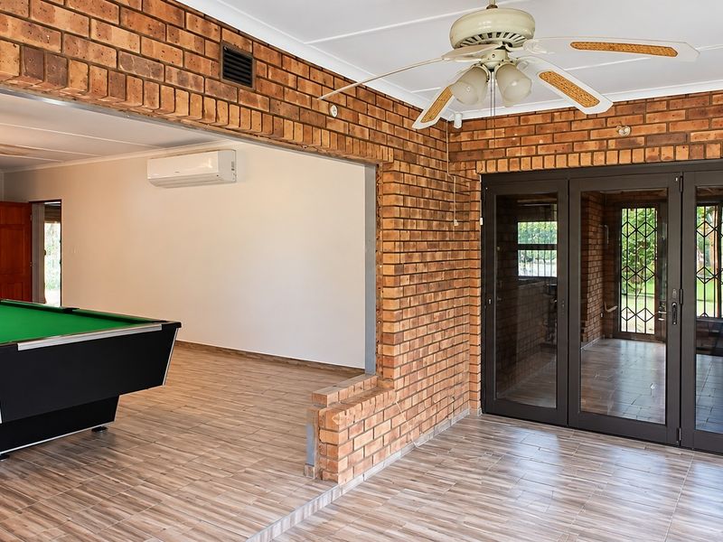 Spacious open-plan living area featuring exposed brick walls, tiled flooring, a ceiling fan, and direct access to the exterior through glass doors.