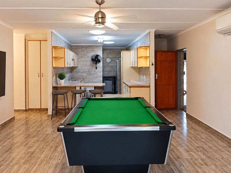Spacious open-plan living area featuring tiled flooring, a modern ceiling fan, split-system air conditioning, and a functional kitchen with built-in cabinetry and breakfast bar.
