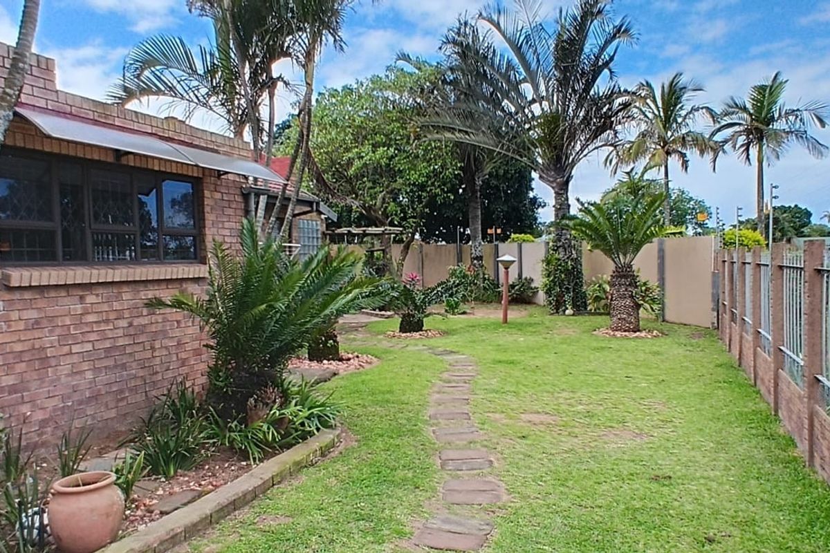 A side garden view featuring a face brick exterior wall, paved pathway, and secure perimeter fencing with electric security wires.