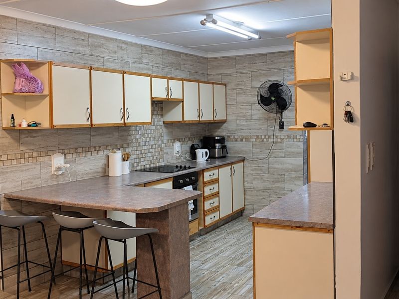 Functional kitchen featuring built-in cabinetry, laminate countertops, tiled backsplash, and integrated oven and hob, with a breakfast bar area.