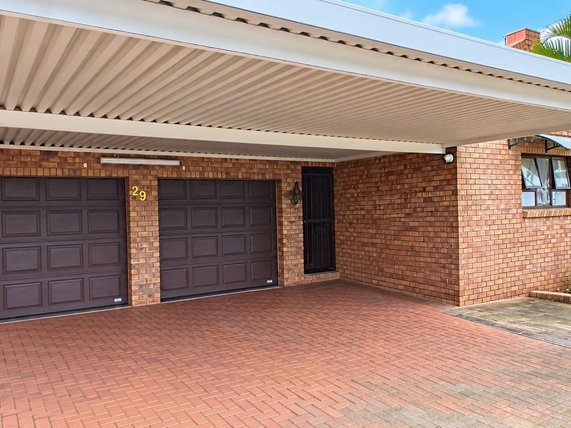 Front exterior view featuring a double garage with a covered carport and paved driveway, showcasing a well-maintained brick facade.