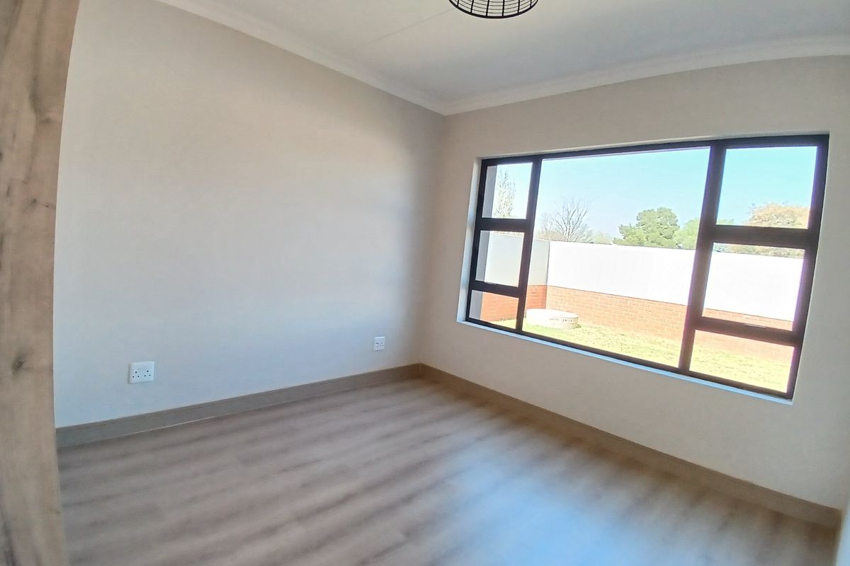 A bright, empty bedroom featuring modern laminate flooring, neutral walls, and a large window providing natural light and a view of the rear garden.