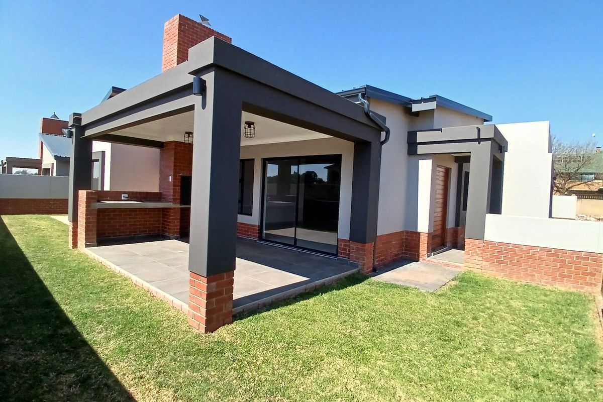 A modern rear exterior view featuring a covered patio with a built-in brick braai, tiled flooring, and sliding glass doors leading into the home.
