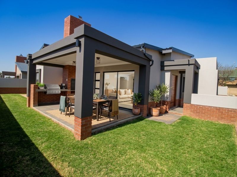 A modern covered patio featuring a built-in braai, brick chimney, and tiled flooring, seamlessly connecting to the interior living space through large sliding glass doors.