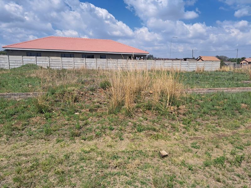 A vacant residential plot featuring a precast concrete boundary wall and natural grass coverage, ready for development.