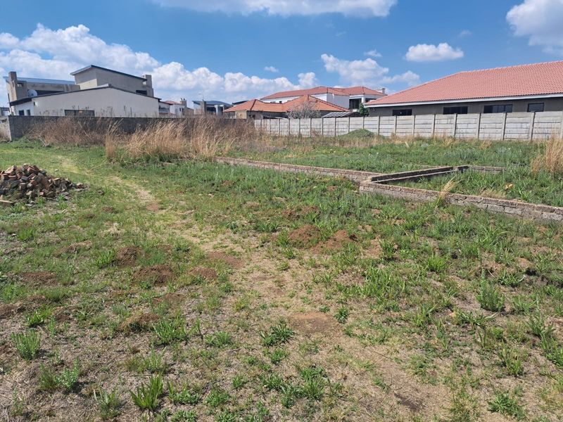 A vacant residential plot featuring a perimeter wall and existing brick foundation work, ready for development.
