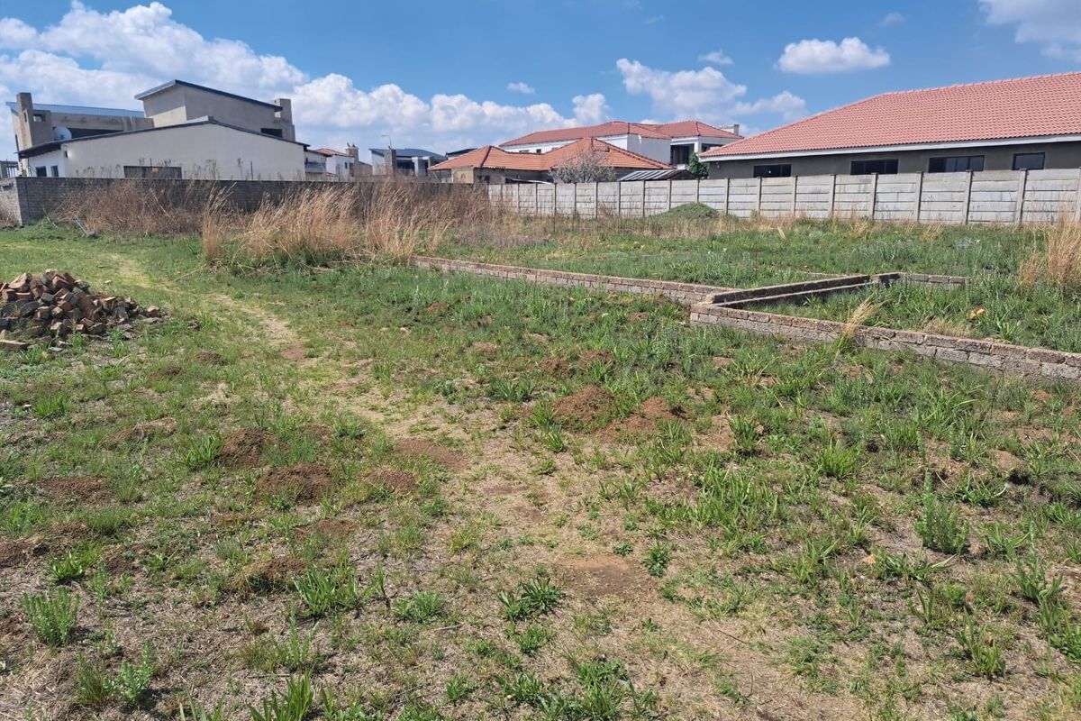 A vacant residential plot featuring a perimeter wall and existing brick foundation work, ready for development.