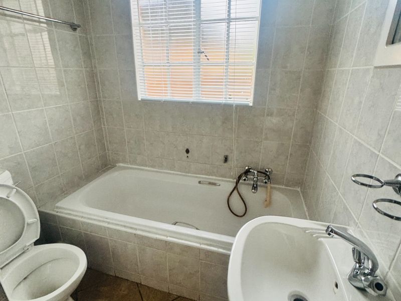 A functional bathroom featuring a built-in bathtub, pedestal basin, and toilet, finished with neutral ceramic wall and floor tiles.
