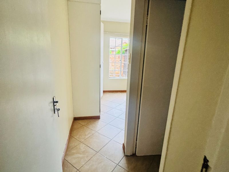A functional hallway featuring tiled flooring and a built-in cupboard, leading towards a windowed area.