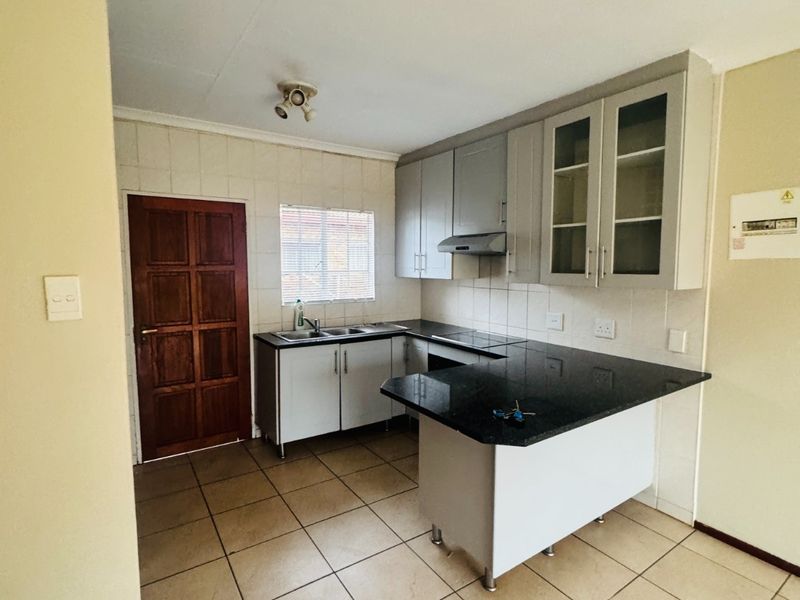 A functional kitchen featuring built-in cabinetry, granite countertops, a tiled splashback, and ceramic floor tiles, offering a clean and practical workspace.