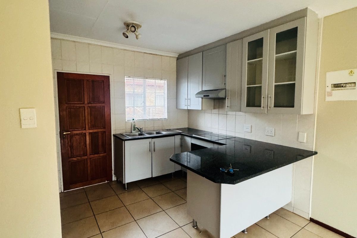 A functional kitchen featuring built-in cabinetry, granite countertops, a tiled splashback, and ceramic floor tiles, offering a clean and practical workspace.